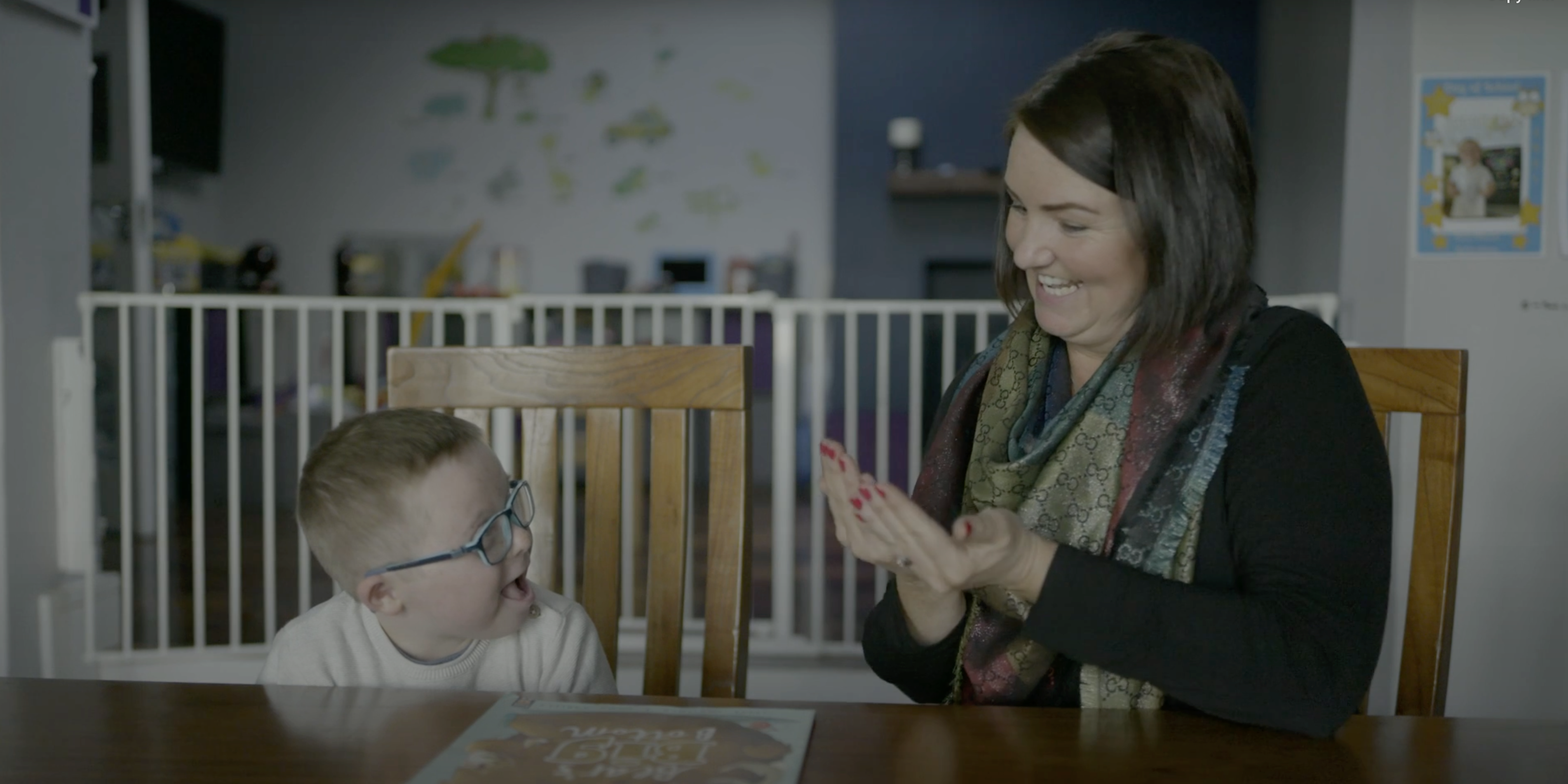 Woman and child sitting at a table in a home setting, possibly playing a game.