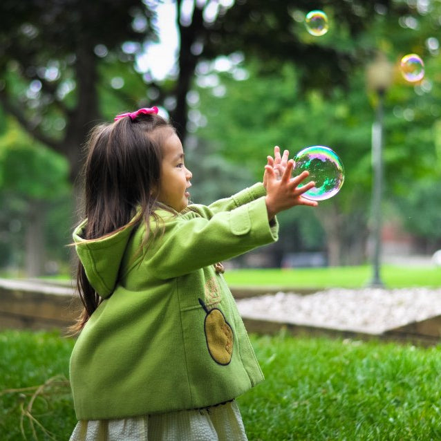 Child in a green coat blowing bubbles in a park