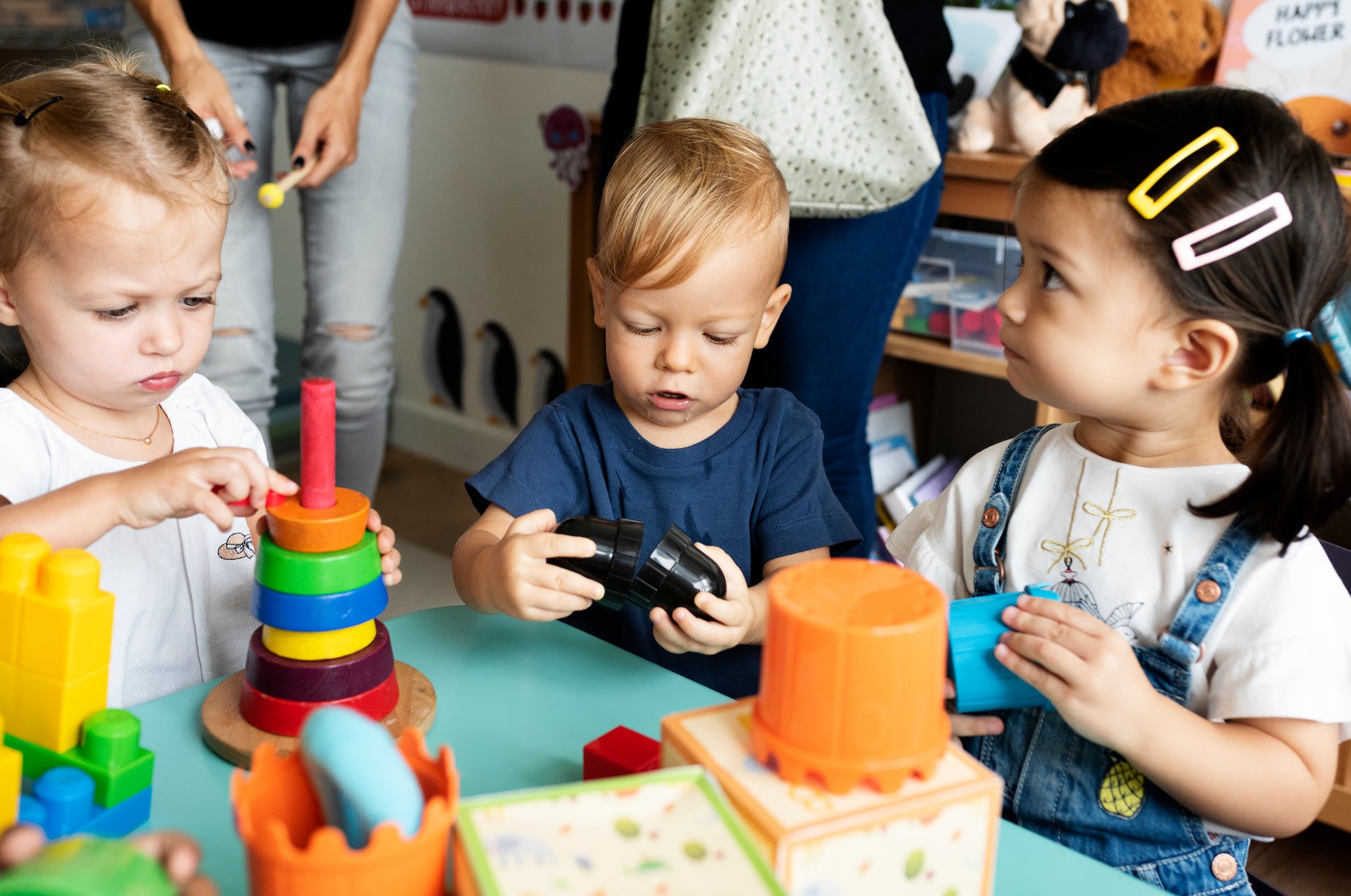 Children playing with colorful toys at a table in a classroom setting.